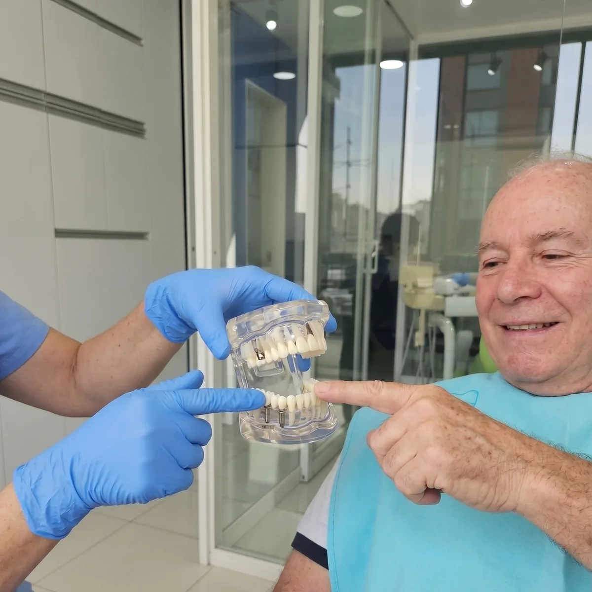 Paciente señalando un modelo dental con implantes junto a la mano enguantada del especialista
