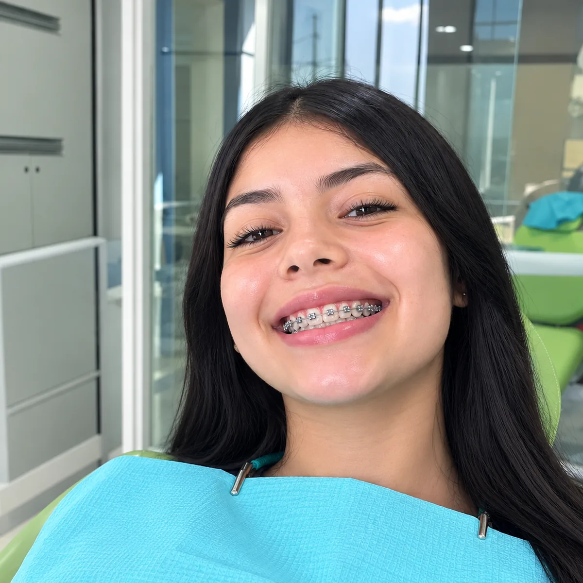 Joven sonriendo con brackets metálicos en el sillón dental